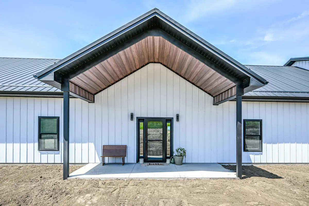 White board-and-batten barndominium with a timber-look gable porch and black trim