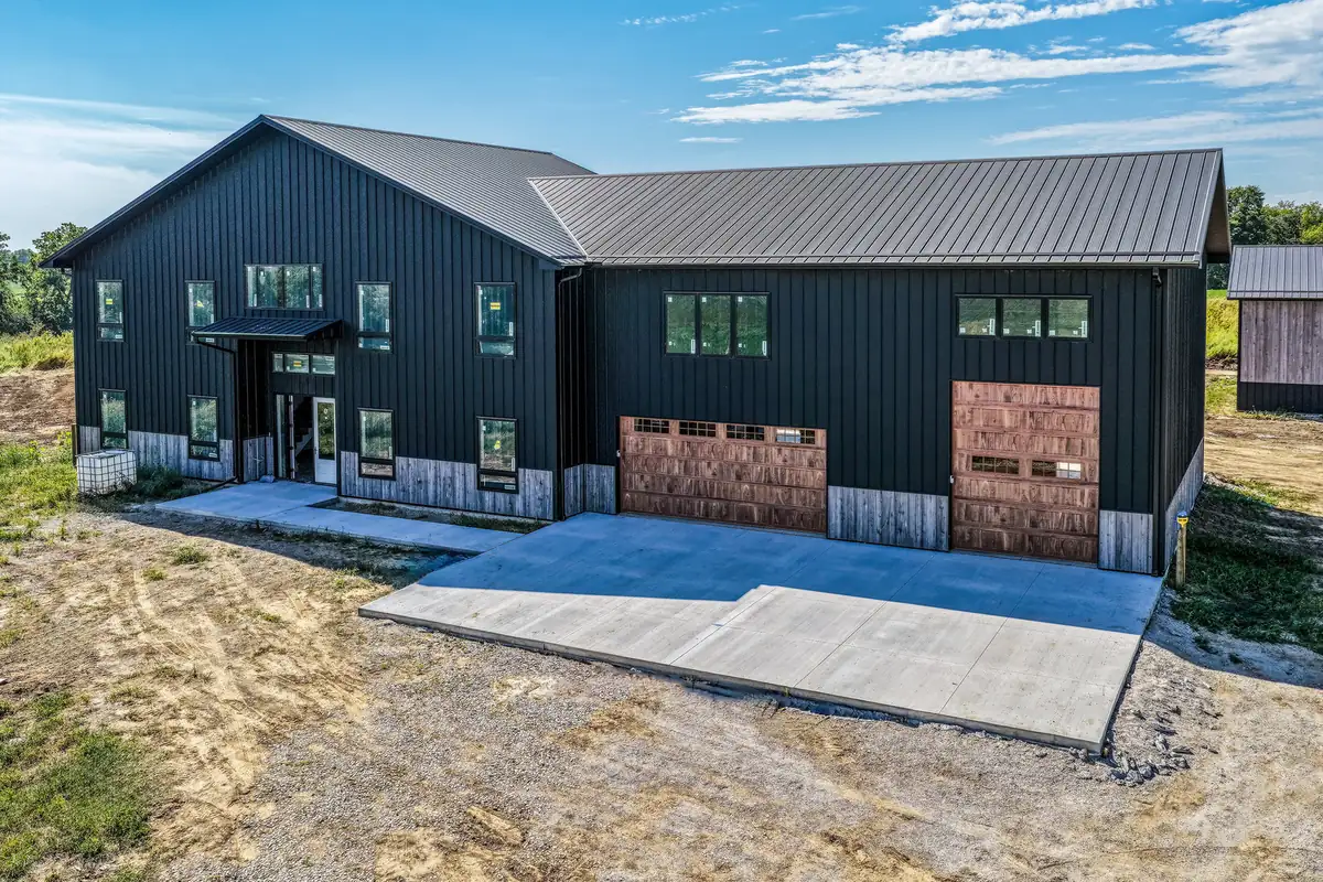 Black steel-sided barndominium with wood-look overhead doors and a concrete apron