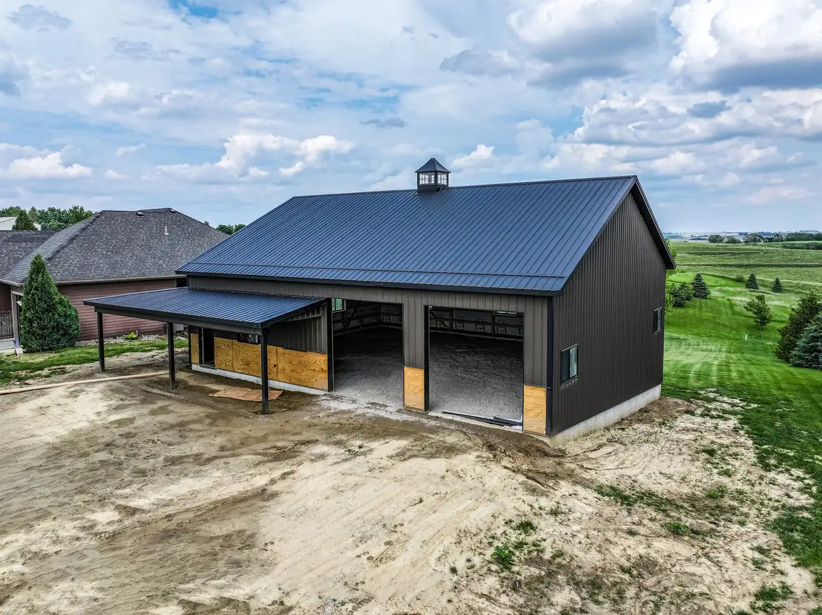Black post frame shop with a covered lean-to and cupola in a residential neighborhood
