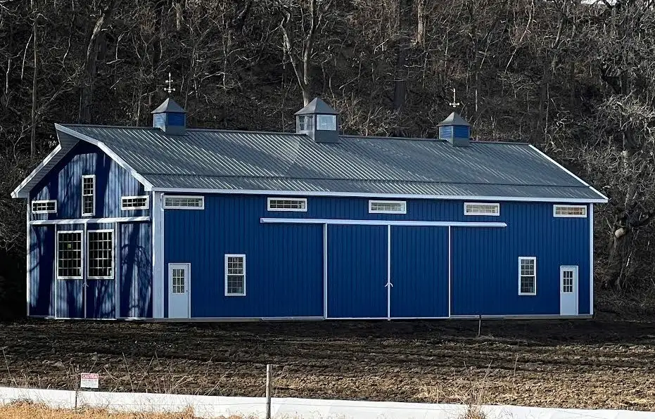 Blue post frame horse barn with white trim and three cupolas