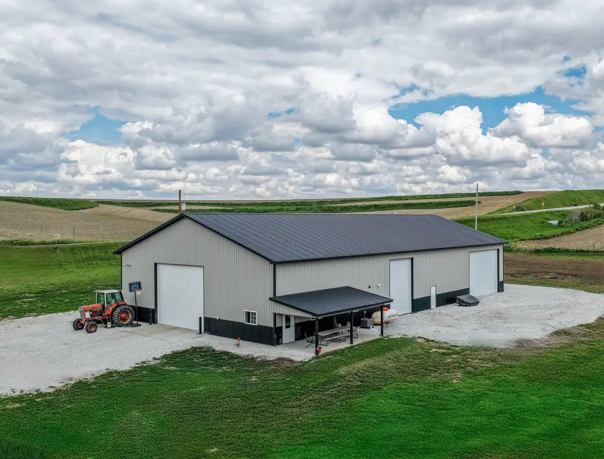 Drone view of a tan post frame farm shop with a lean-to and a red tractor out front