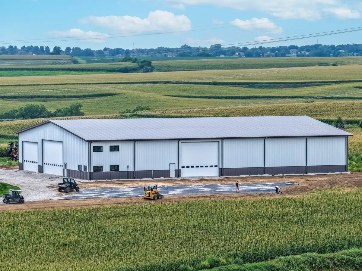 Drone view of a large white post frame machine shed surrounded by cornfields