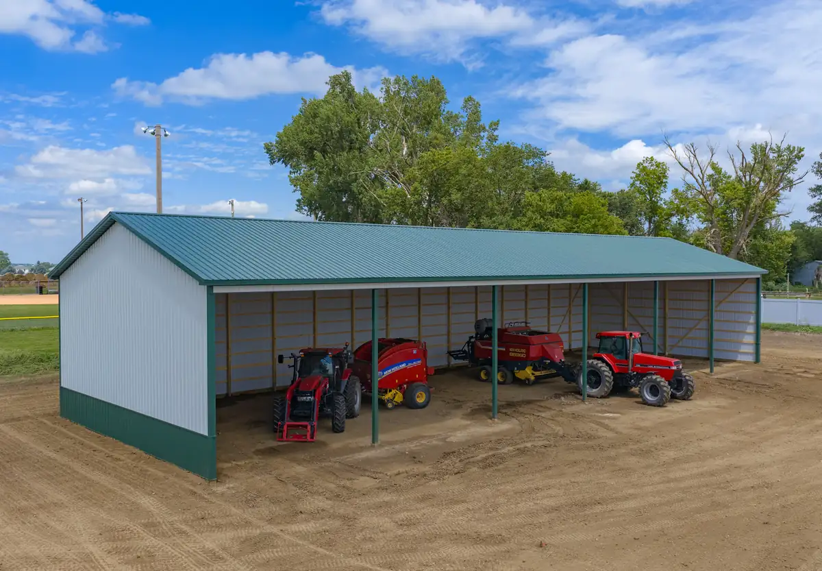 Open-front post frame machine shed with red tractors and hay equipment inside